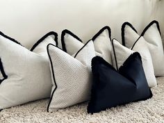 four black and white pillows lined up on the floor in front of a wall with a potted plant