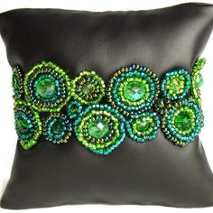 a black pillow with green beaded bracelets on the front and back of it