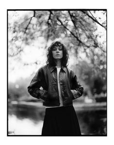 a black and white photo of a woman standing in front of a tree with her hands on her hips