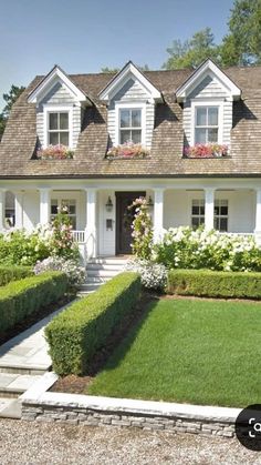 a white house with lots of windows and flowers in the front yard, surrounded by greenery