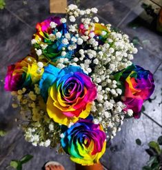 a bouquet of colorful roses in someone's hand on the ground with other flowers