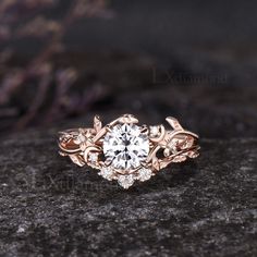 a close up view of a diamond ring on top of a black stone surface with purple flowers and leaves around it