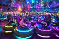 people are sitting on bean bag chairs in an indoor area with colorful lights above them