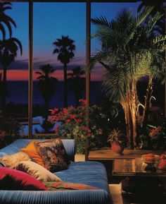 a living room filled with lots of furniture next to tall windows and palm trees in the background