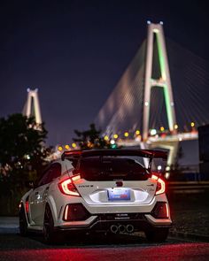 the rear end of a white sports car parked in front of a bridge at night