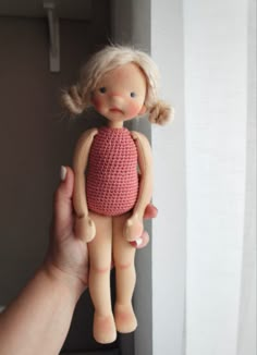 a hand holding a doll in front of a window