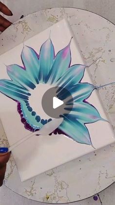 a person is painting a flower on a white plate with blue and purple flowers in the center