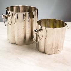 two silver pots sitting on top of a white counter next to each other and one is empty