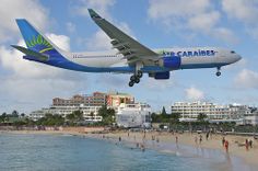 an airplane is flying over the beach with hotels in the background and people swimming in the water