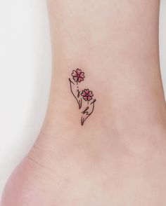 a small flower tattoo on the side of a woman's ankle, with pink flowers