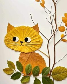 a cat made out of leaves on top of a white surface with branches and leaves around it