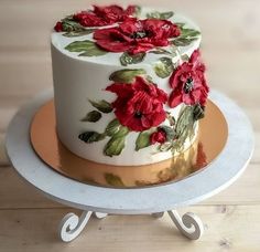 a white cake with red flowers on it sitting on top of a wooden table next to a plate