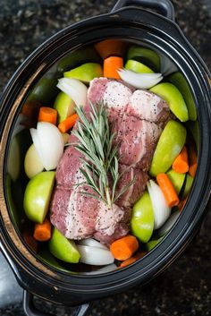 meat and vegetables in a slow cooker with seasoning sprig on top