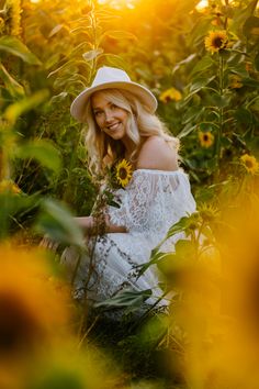 a beautiful blonde woman sitting in the middle of a sunflower field wearing a white hat