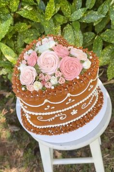 a chocolate cake with pink and white flowers on top sitting on a table in front of some bushes