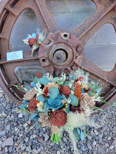 a bouquet of flowers sitting on the ground next to a rusty wheel with some writing on it