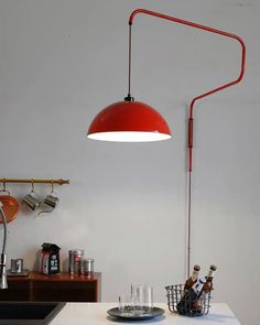 a red lamp hanging from the ceiling over a kitchen counter with wine glasses and utensils on it