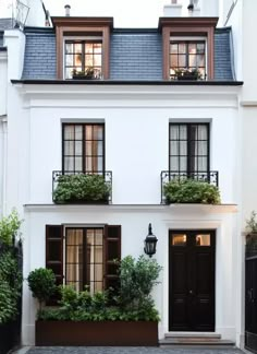 a white house with black shutters and plants on the front window sill,