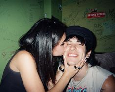 a man kissing a woman on the cheek in front of a wall with writing all over it