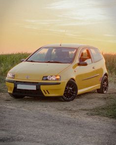 a small yellow car parked in front of a corn field