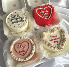 four heart shaped cakes in plastic containers on a white cloth covered table with the words happy valentine's day written on them