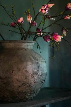 a vase with pink flowers in it sitting on a table next to a blue wall