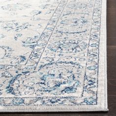 a white and blue rug with an ornate design on the bottom, in front of a wooden floor