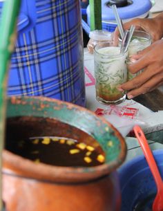 a person holding a glass filled with liquid next to a potted plant and other pots