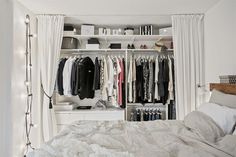 an open closet with clothes hanging on the shelves and lights strung from the ceiling, in front of a bed