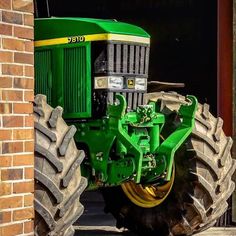 a green tractor parked next to a brick building