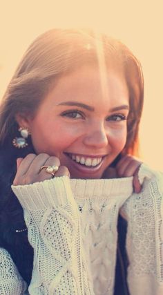 a woman smiling and holding her sweater over her shoulder with the sun shining behind her