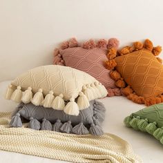 four pillows with tassels on them sitting on a white surface next to a blanket