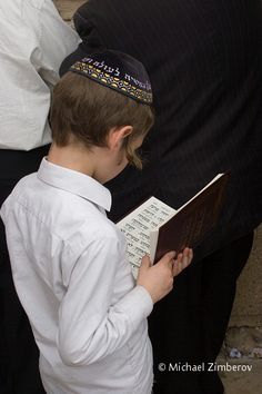 a young boy is reading a book while wearing a jewish hat and holding it in his hands