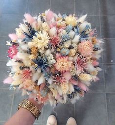 a person holding a bouquet of flowers in their hand on the tile floor next to a pair of white shoes