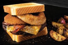 a grilled cheeseburger with bacon and potatoes on a black plate next to it