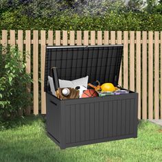 an outdoor storage box sitting in the grass next to a wooden fence and shrubbery