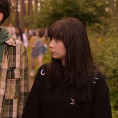 a man and woman standing next to each other on a forest path with trees in the background