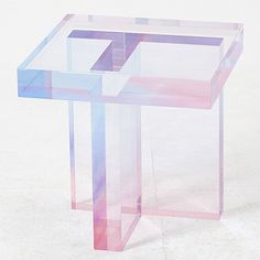 a pink and blue glass table sitting on top of a white floor next to a wall