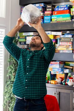 a man holding up a plastic bag in front of his face while standing next to a book shelf filled with books