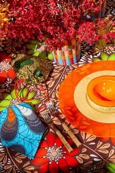 an orange plate on a colorful table cloth with red flowers in vases behind it