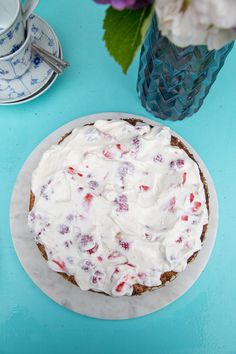 a cake with white frosting sitting on top of a blue table next to flowers