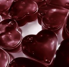 many heart shaped chocolates are shown in this close up photo, with one being filled with liquid