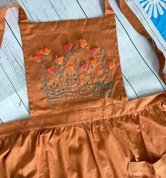 an orange apron with flowers on it sitting on a wooden floor next to a blue and white wall