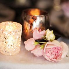 two pink roses sitting on top of a table next to a lit candle and a cup