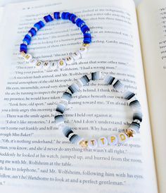 a blue and white beaded bracelet sitting on top of an open book with words written in gold