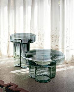 two glass tables sitting on top of a carpeted floor next to a potted plant