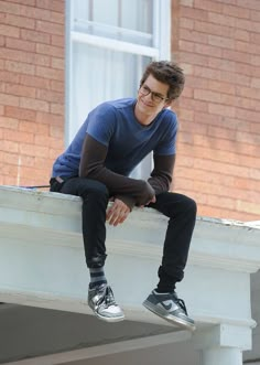 a man sitting on top of a white ledge next to a brick building with his legs crossed