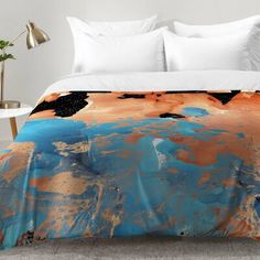 an orange and blue comforter on a bed in a room with white walls, flooring and furniture