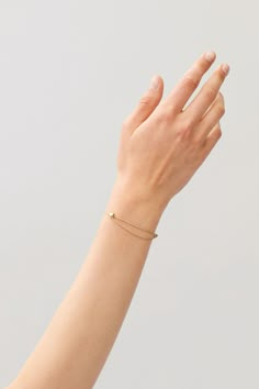 a woman's hand with a tiny gold bracelet on her left wrist and the other hand in the air