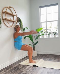 a woman in a blue swimsuit is doing yoga on a mat near a potted plant